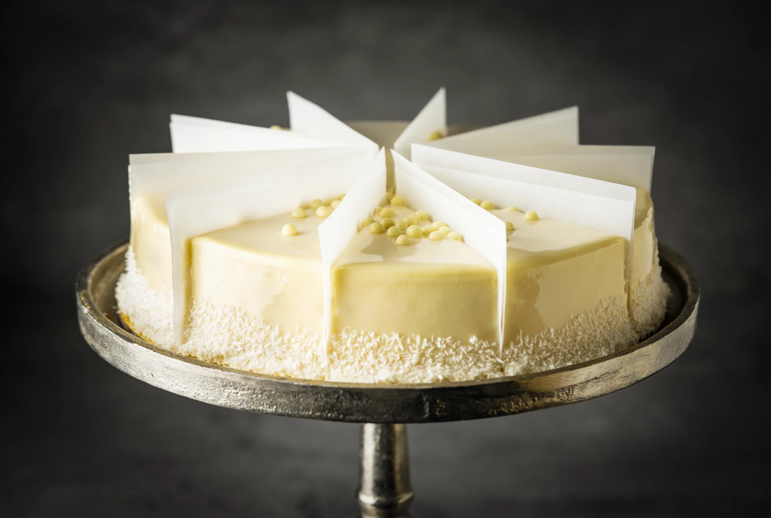 Pre-Sliced Raffaello Cake - Delightful white chocolate and coconut cake, elegantly pre-sliced and topped with white chocolate pearls.